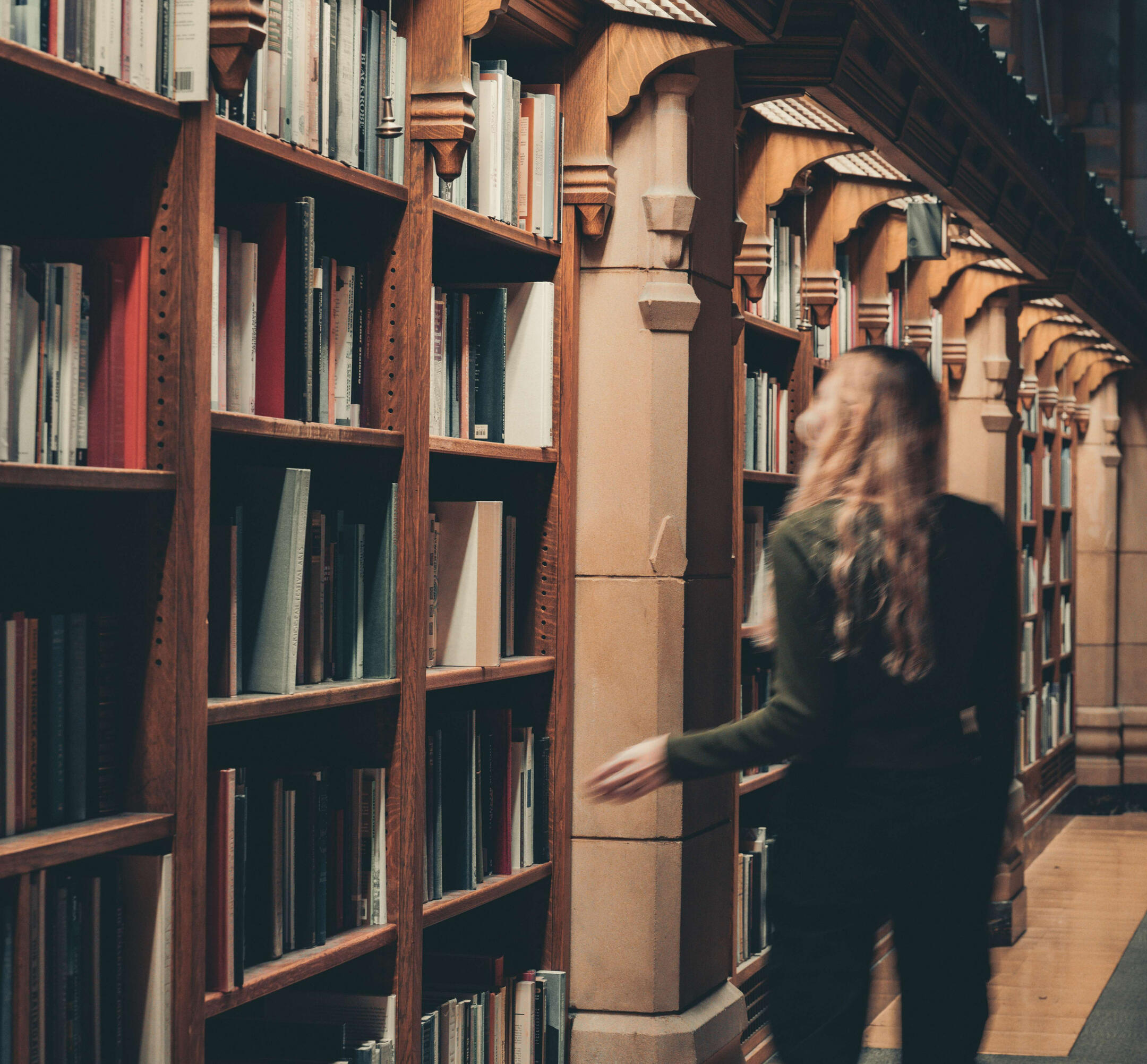 A woman walks alongside bookshelves in a library. Her back is to the camera. Photo credit to: https://www.instagram.com/hello_meagain/
